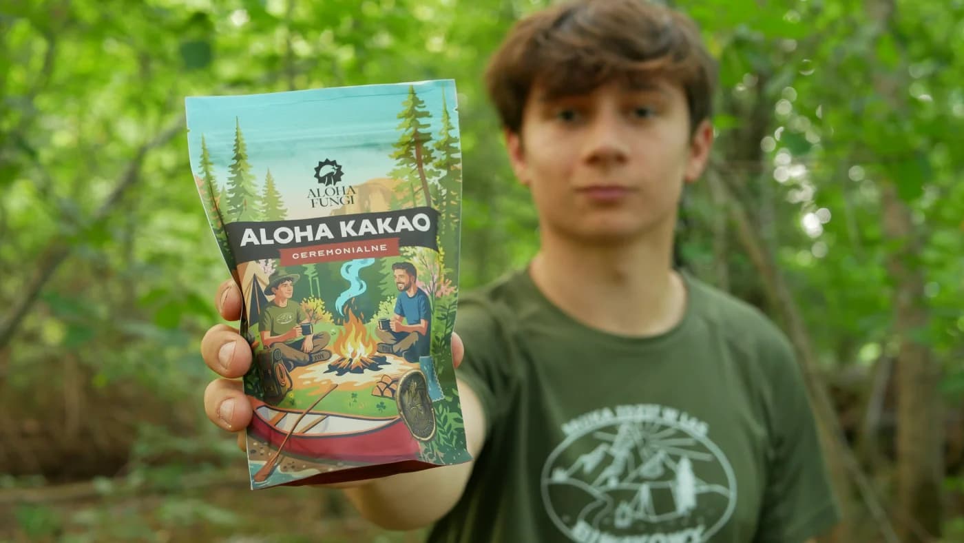 Mężczyzna w lesie trzyma torebkę Aloha Kakao Ceremonialne z ilustracją biwaku przy ognisku.